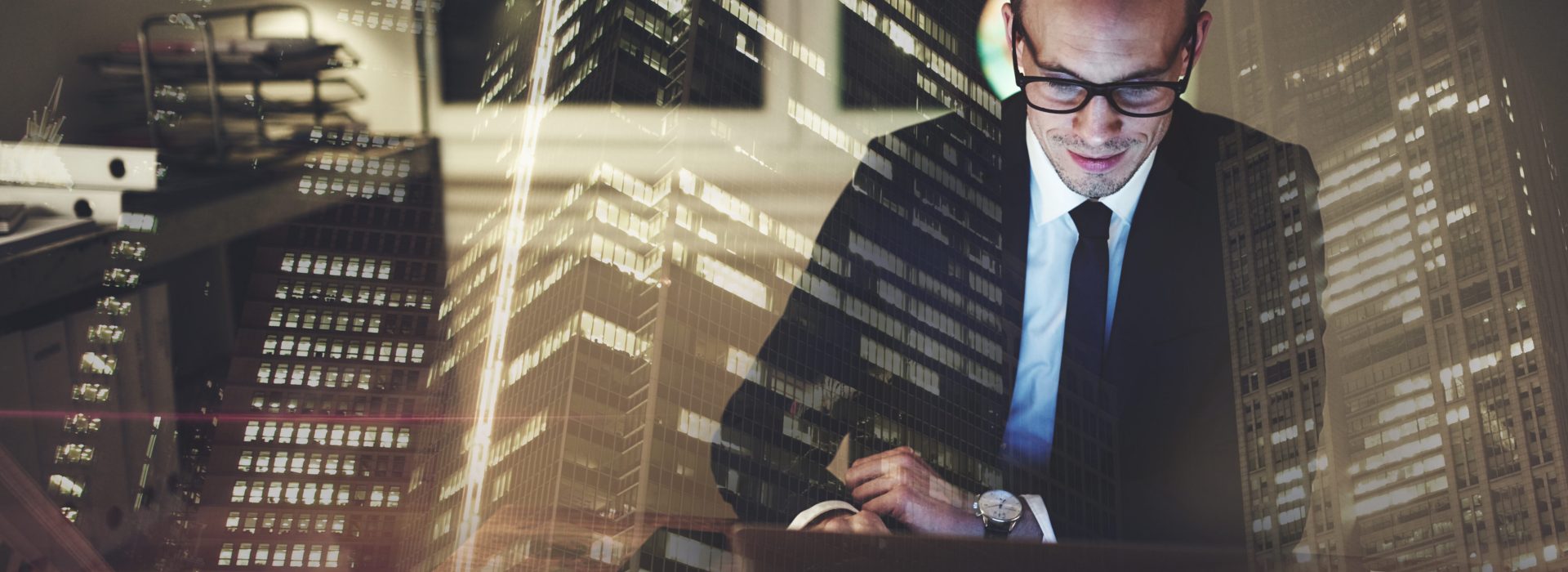 Optimistic businessman working on laptop at office in the night, Working overtime with big city in background