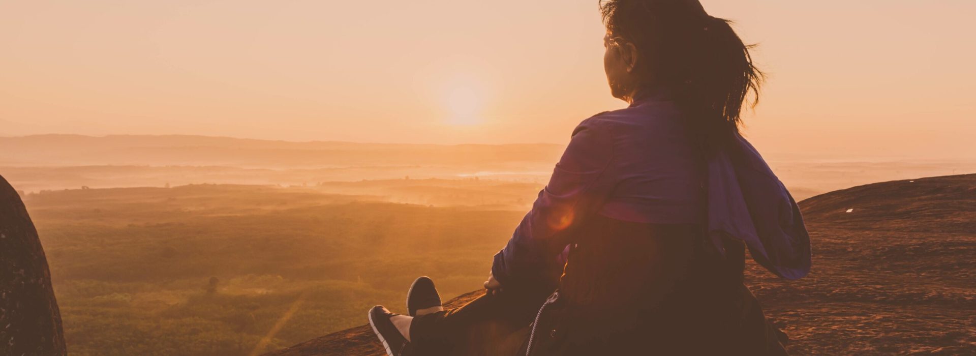 Young woman sitting on peak hill lookup mountain and forest at morning sunlight background. Happy gril relaxing concept.